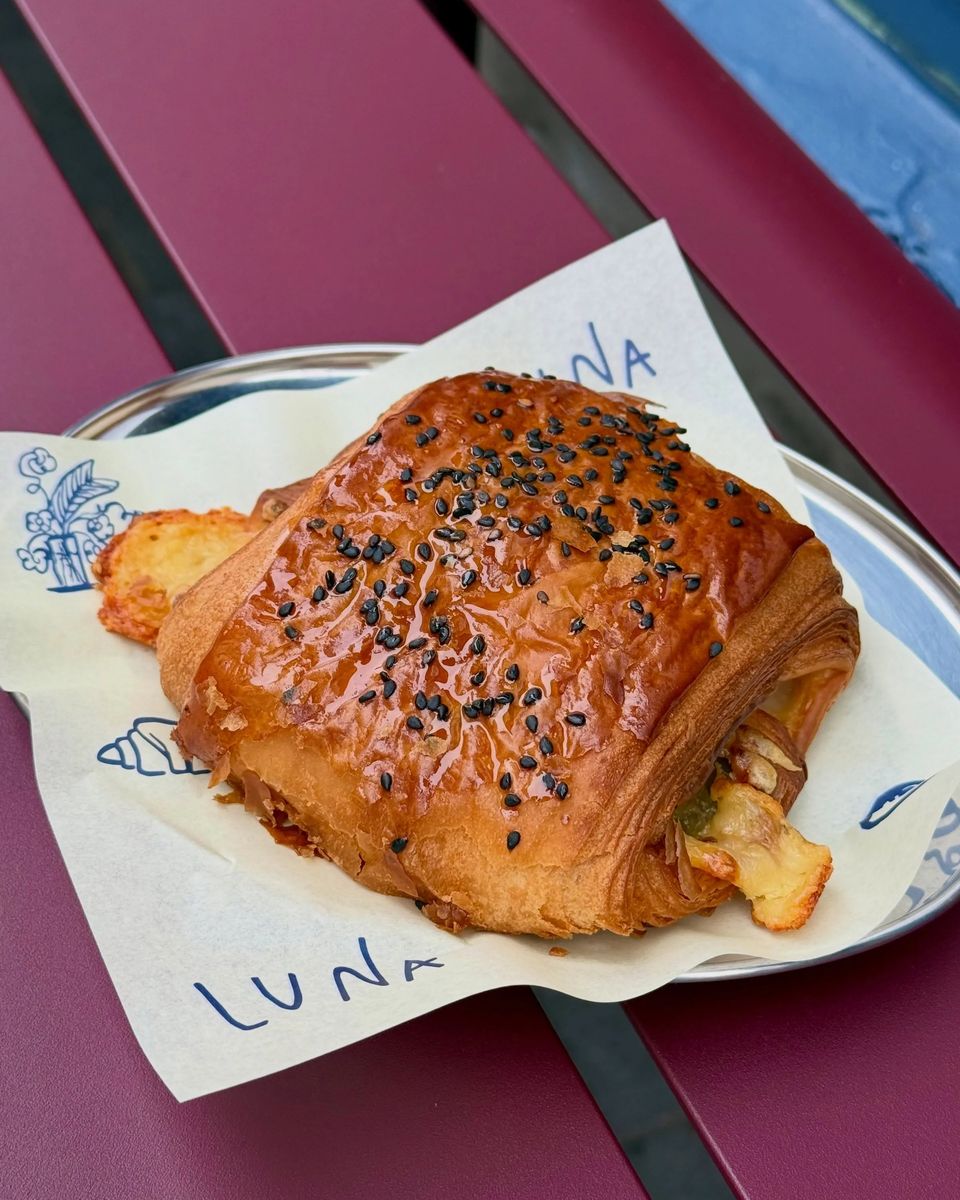 A savoury pastry on LUNA-printed paper, on a maroon bench
